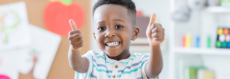 Child smiling and giving two thumbs-up
